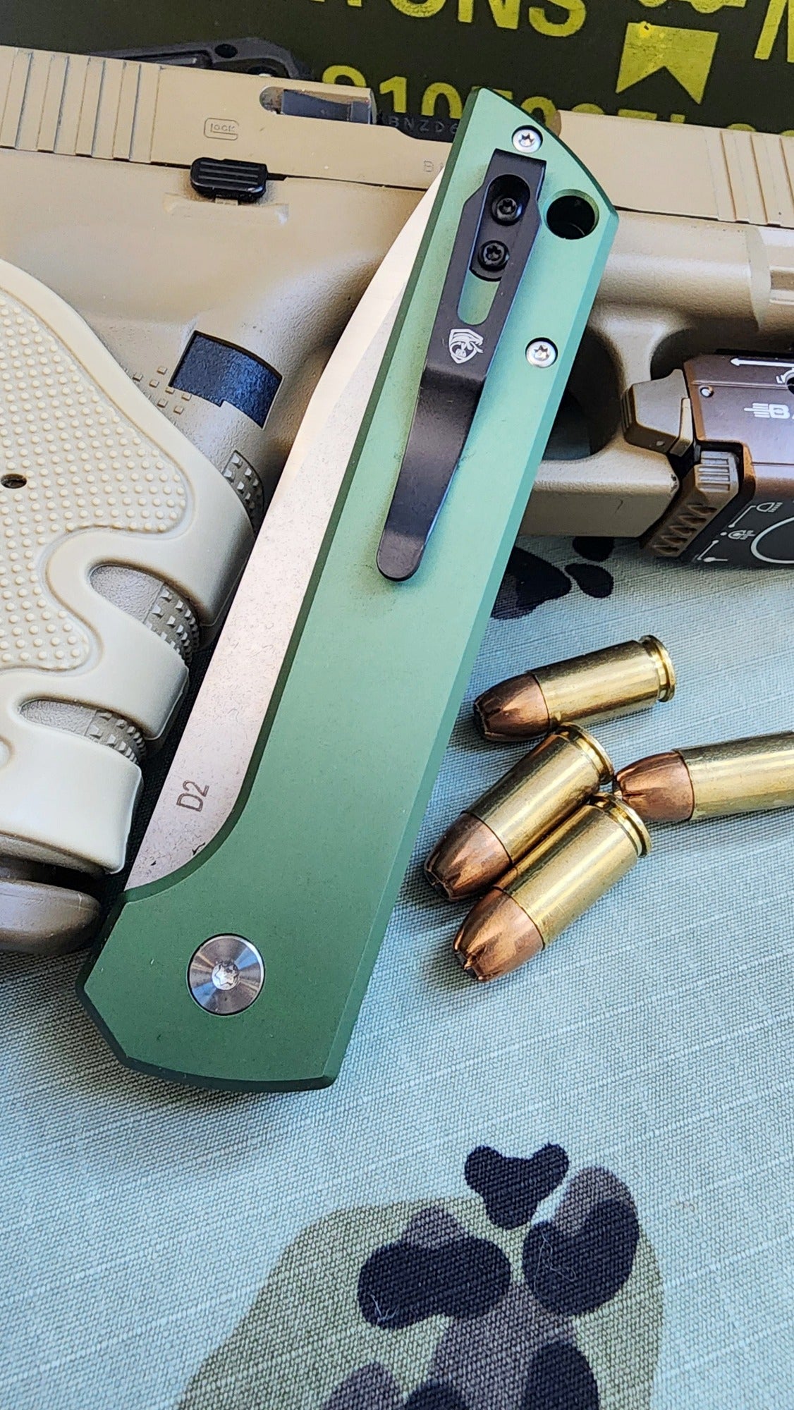 Green folding knife with bullets and a gun on a textured surface