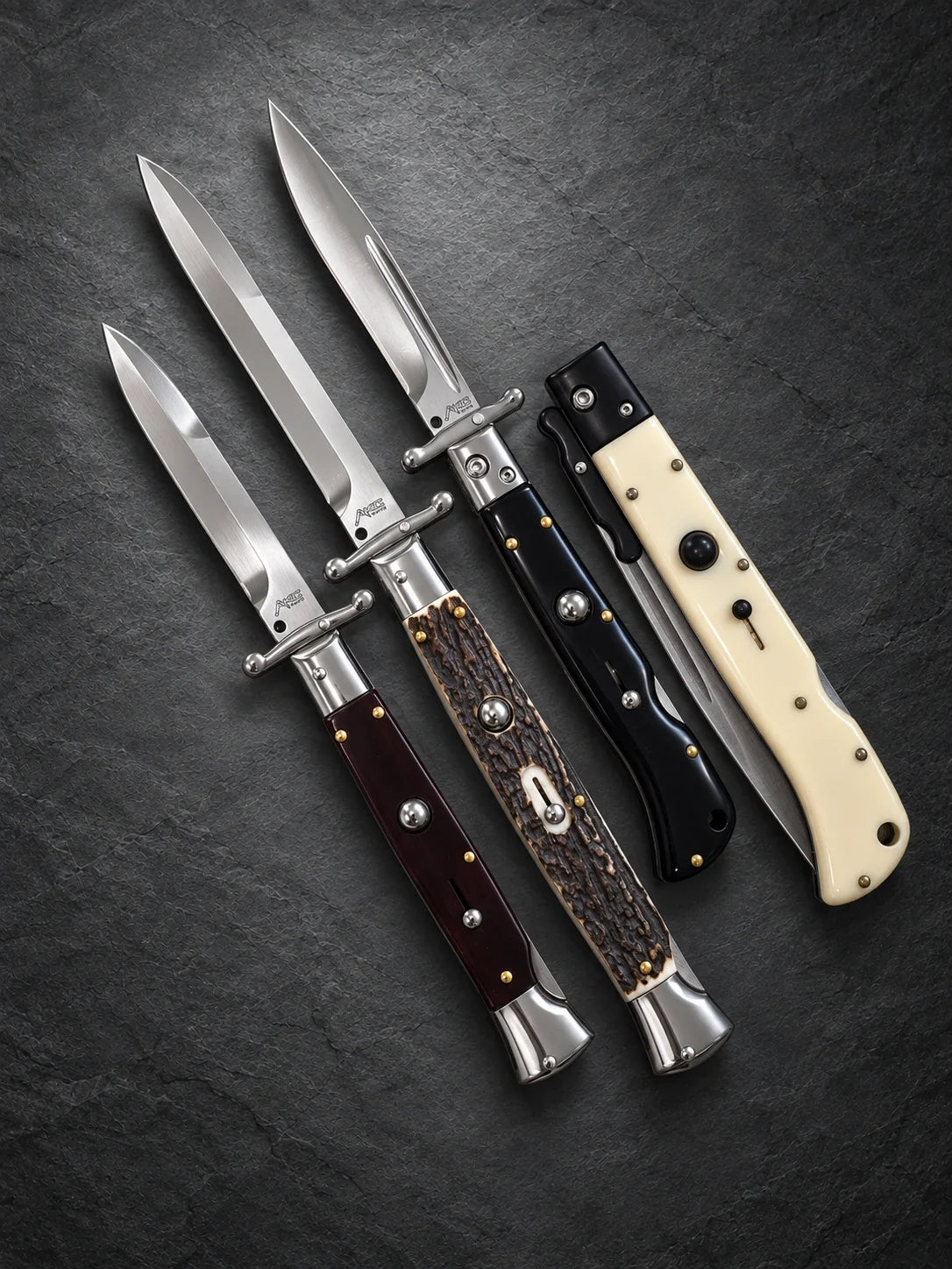 4 Italian swinguard switchblade knives with dark wood-look, stag-style, black and ivory-style handles on a charcoal background.