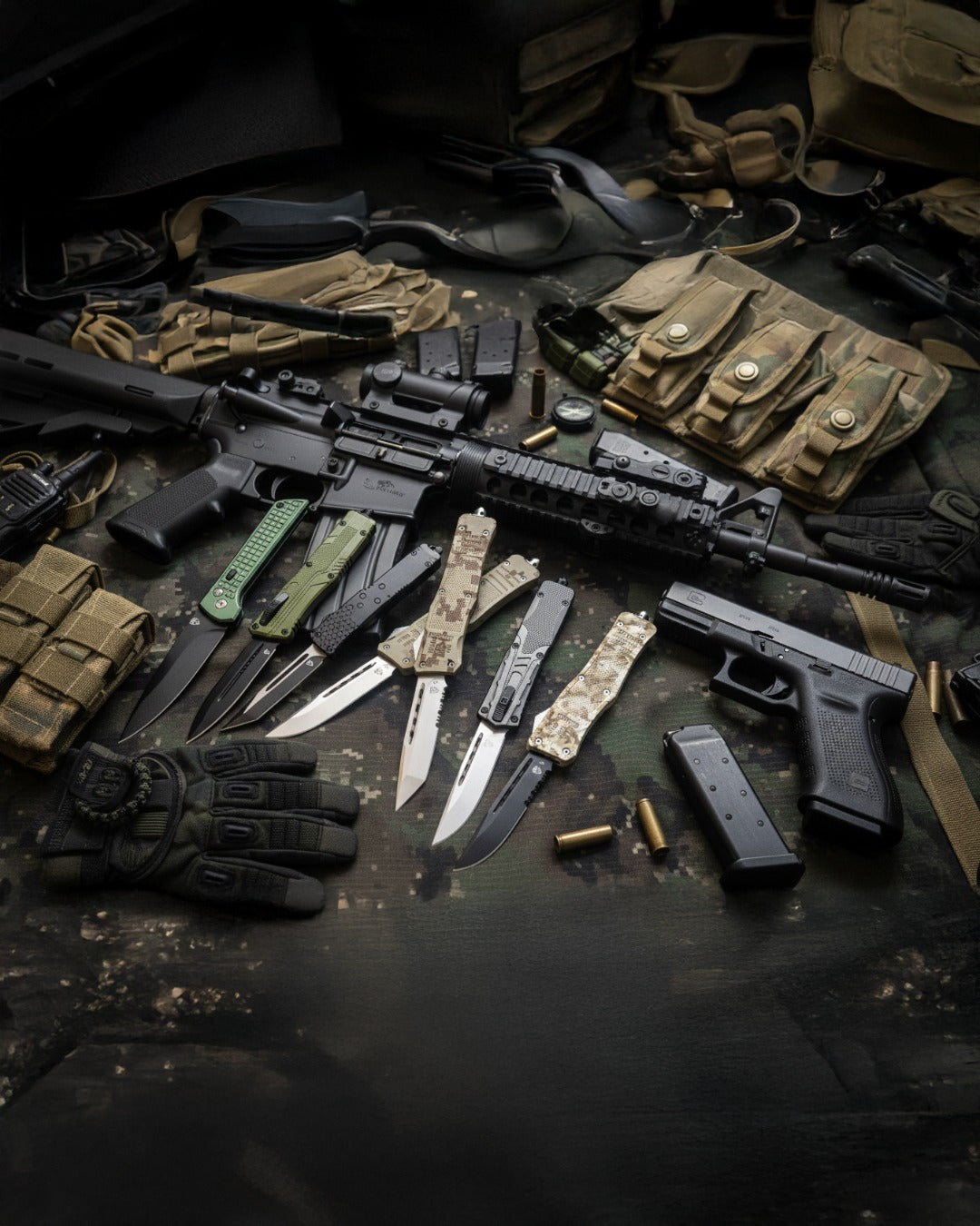Group of automatic knives for sale on a dark cloth surrounded by tactical gear