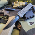 OTF knife with tactical rifle on a camouflage surface