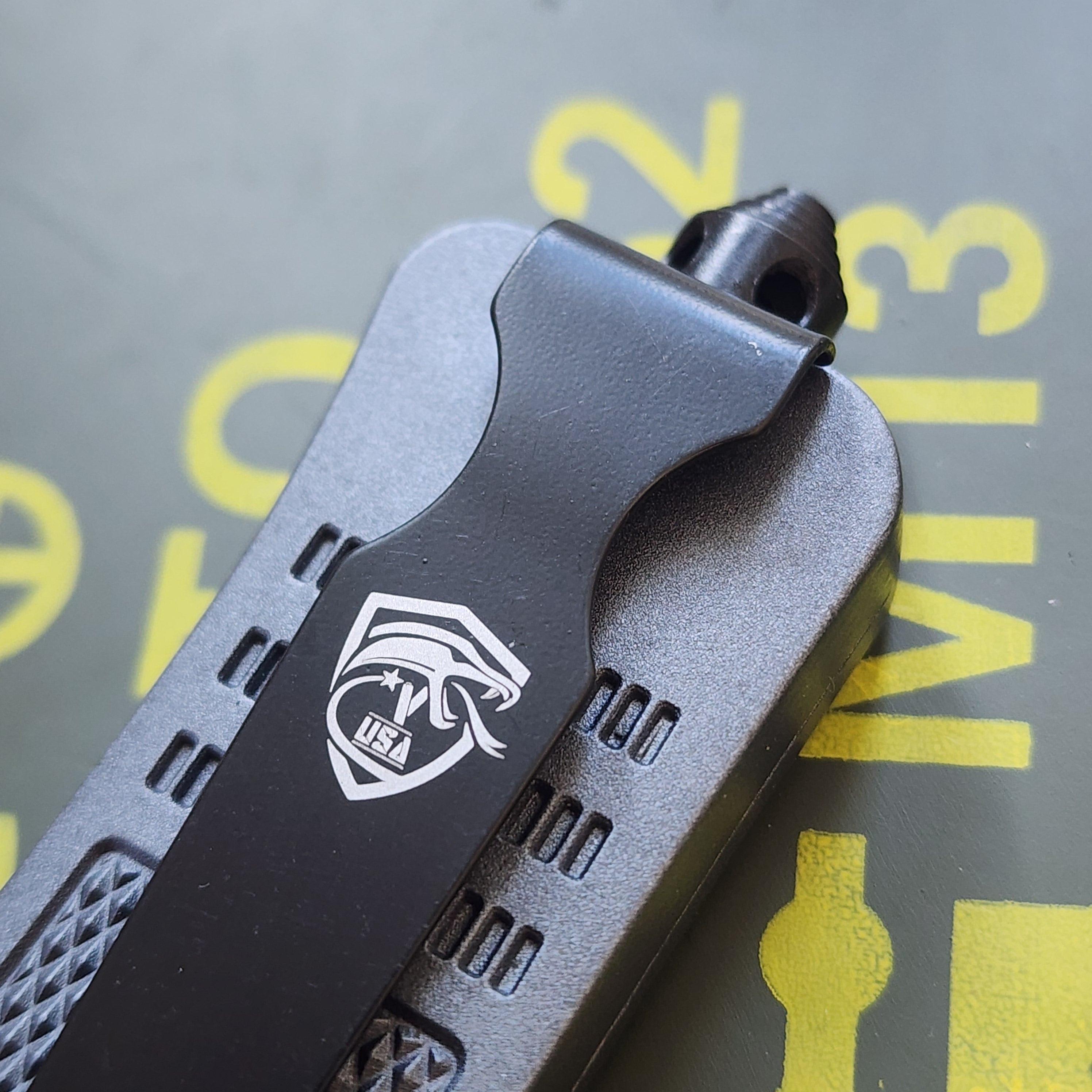 Close-up of a black tactical knife handle with a logo on a blurred background