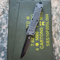 military Gray OTF knife on a green military-style box with text and symbols.