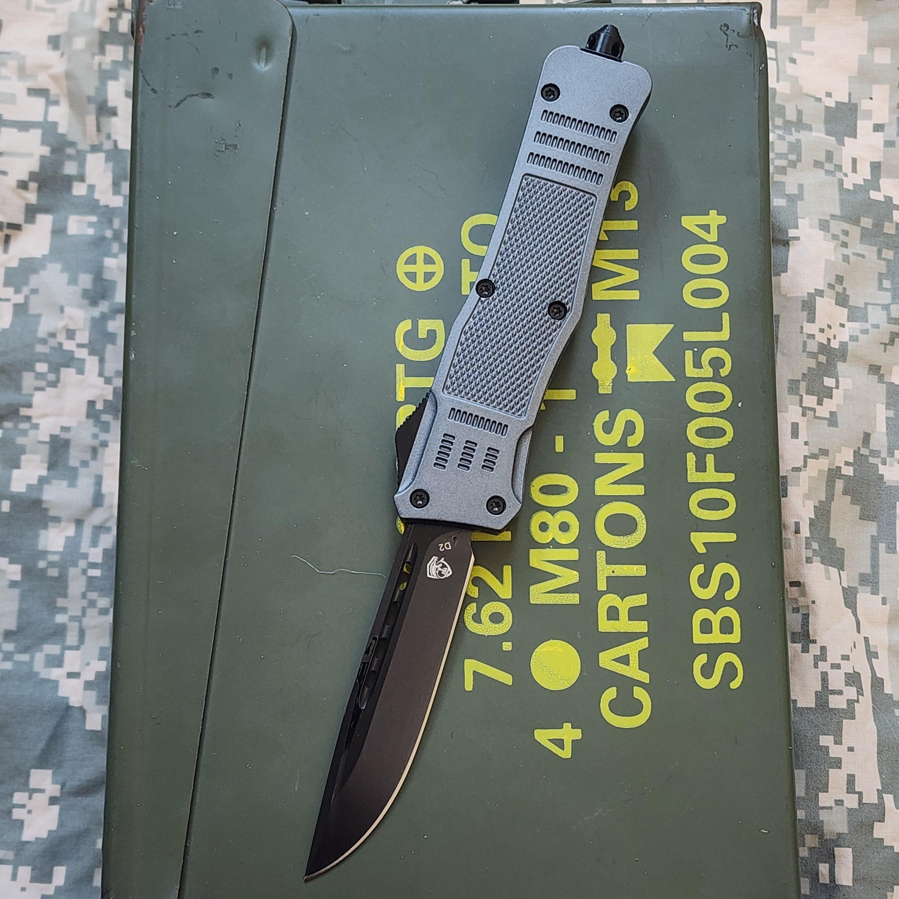 military Gray OTF knife on a green military-style box with text and symbols.