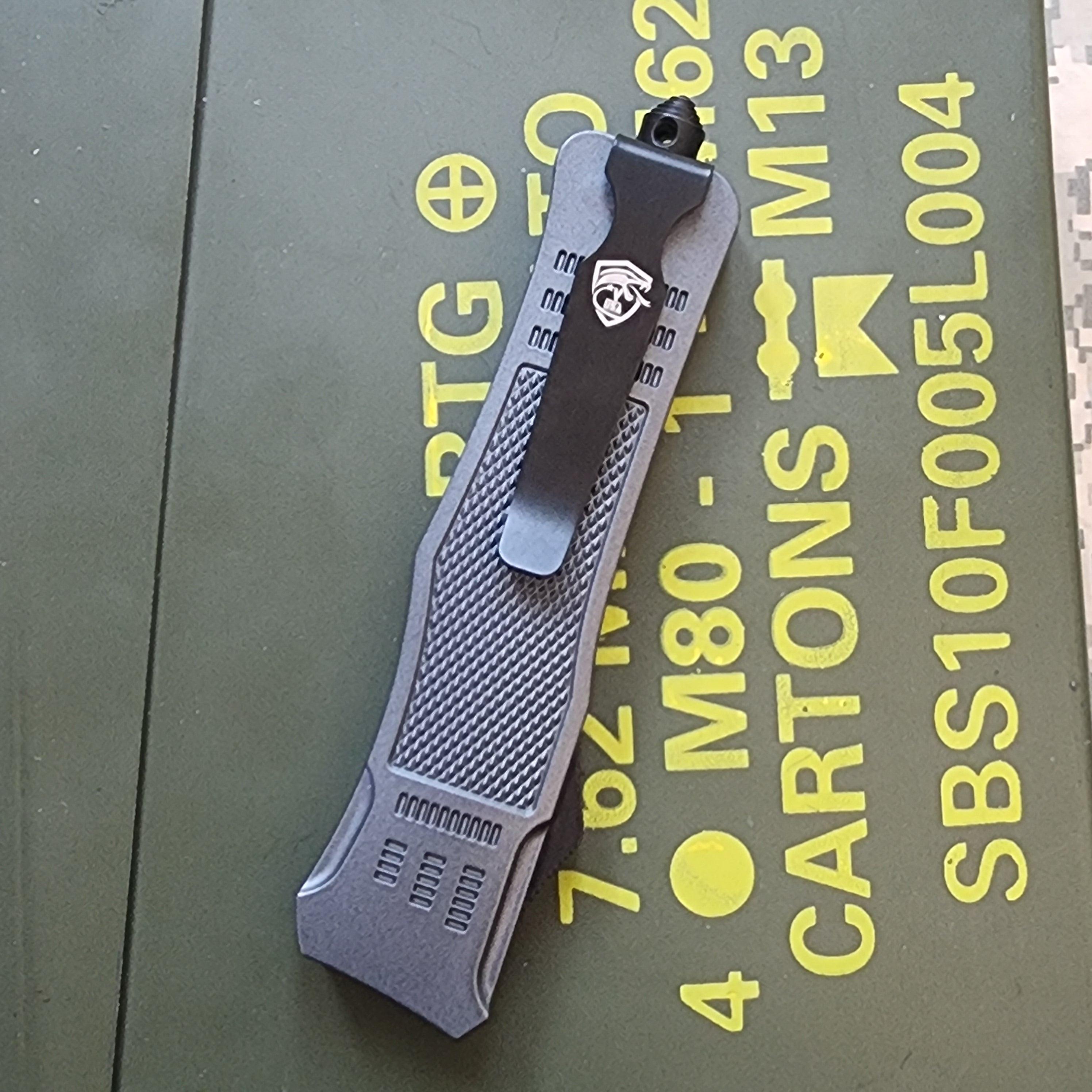 Gray tactical knife on a green surface with yellow text in the background