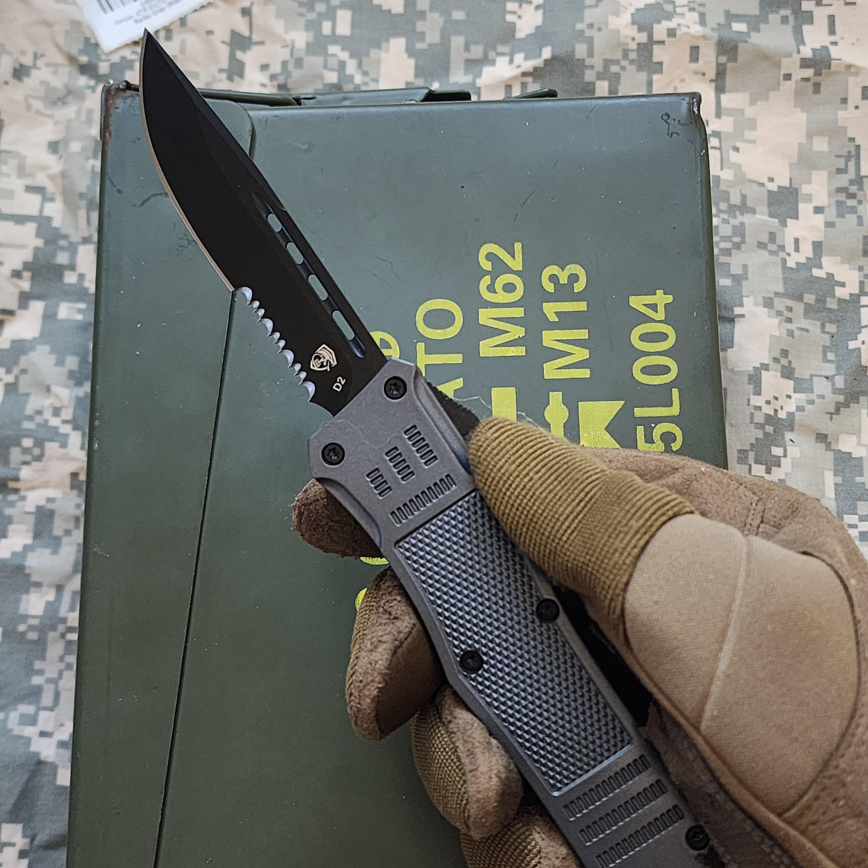 Folding knife held by a gloved hand on a camouflage background