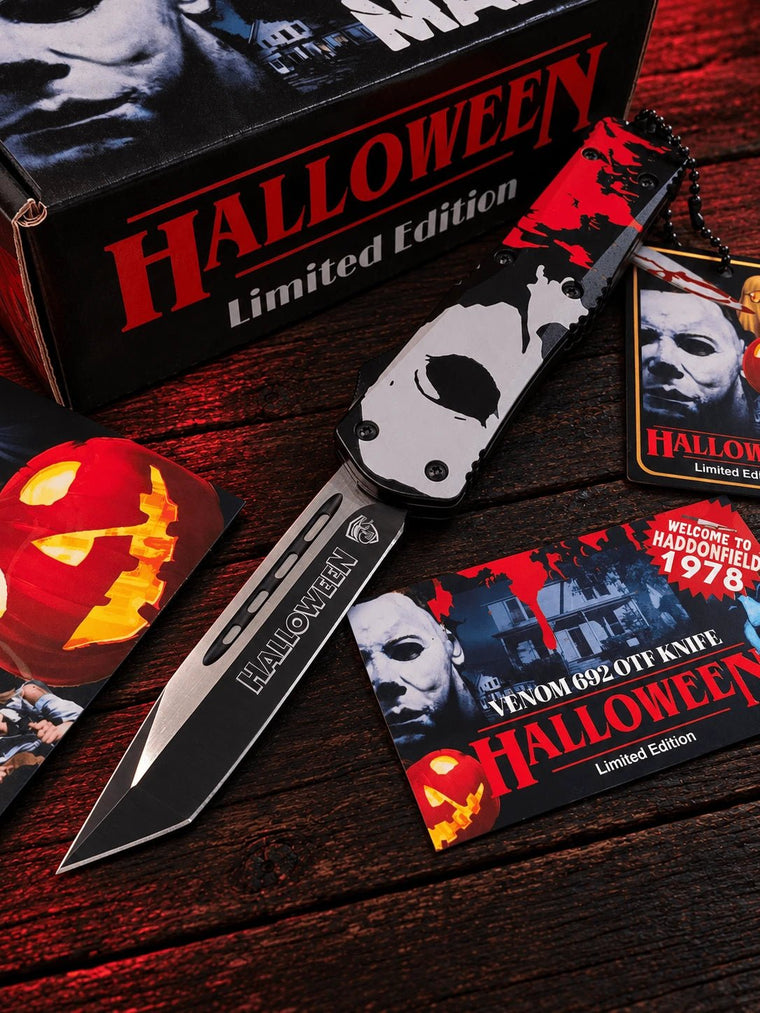 A Venom 602 OTT Knife in a Halloween Limited Edition, shown open on a dark wooden surface with its packaging box, keychain, and themed cards.