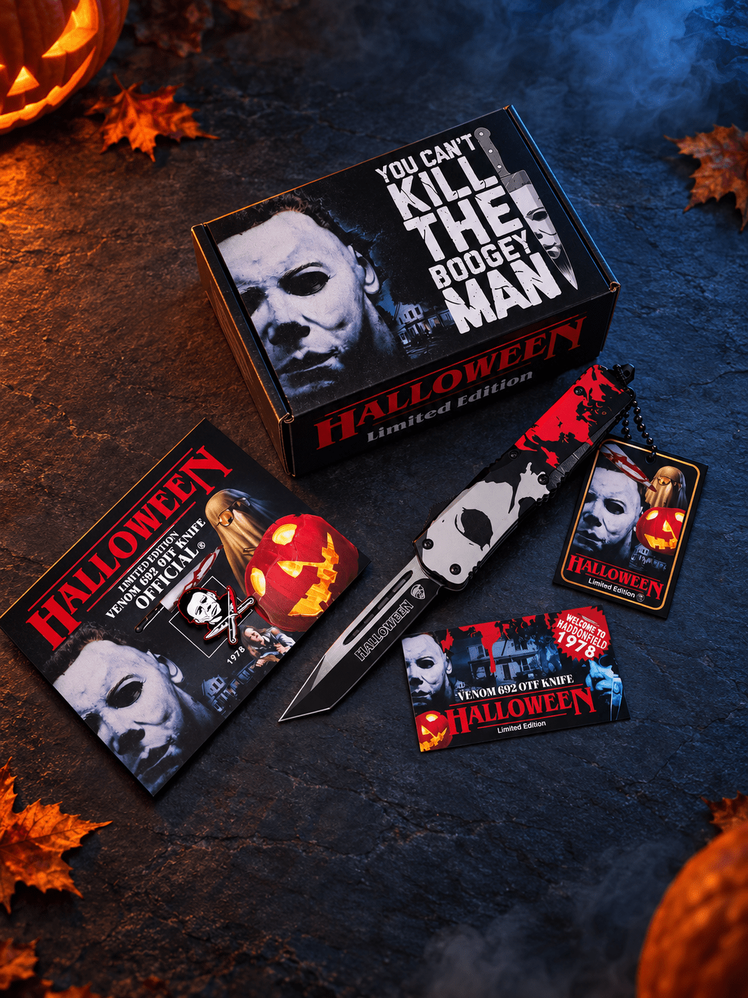 Halloween-themed limited edition knife set displayed on a dark textured surface with autumn leaves and pumpkins. The set includes a boxed knife, a folding pocket knife, a branded card, and a tag, all featuring Michael Myers artwork and red-and-black Halloween graphics.