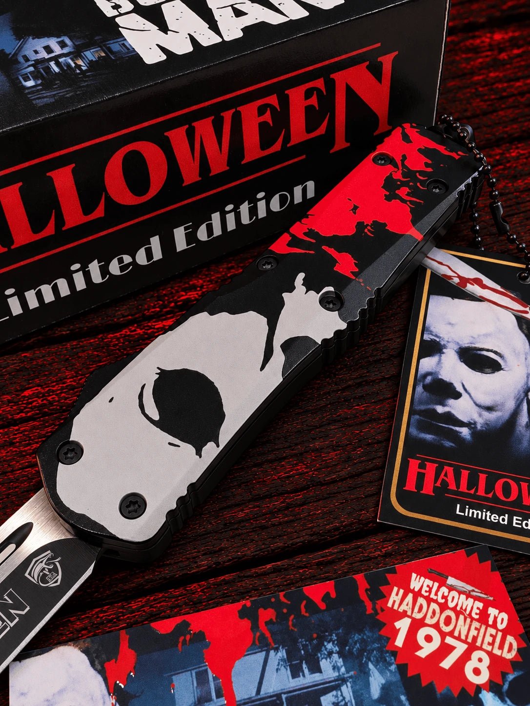 A Halloween-themed limited edition folding pocket knife with a Michael Myers design, displayed next to its packaging and themed accessories on a dark wooden surface.