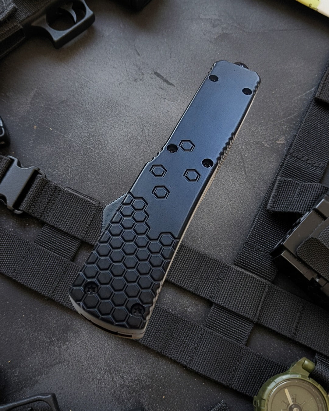 Black tactical knife with honeycomb pattern on a dark surface